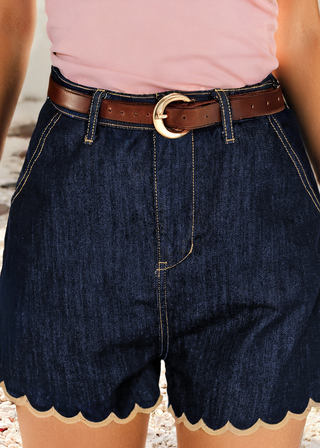 Person wearing a pink top and dark denim shorts with scalloped hem on a blurred background