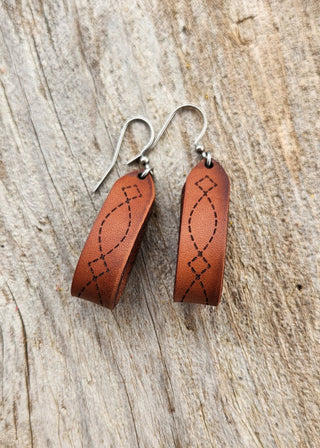Pair of brown leather earrings with fish designs on a wooden surface