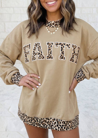 A woman wearing a beige crewneck sweatshirt with 'FAITH' printed across the chest in leopard print letters, featuring matching leopard print trim on the collar, cuffs, and hem.