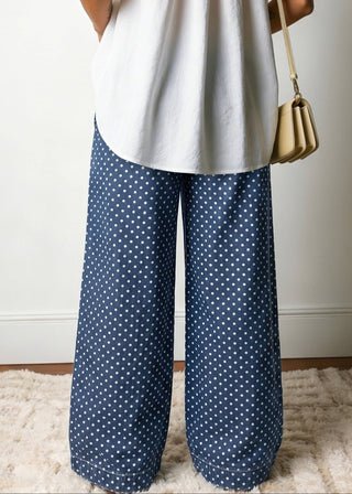 Person wearing a white sleeveless top and blue polka dot pants, standing on a light-colored rug.