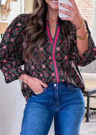 Woman wearing a floral blouse with a pink zipper and blue jeans indoors.