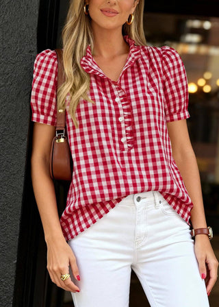 Woman wearing a red and white checkered shirt with white pants, standing against a dark background.