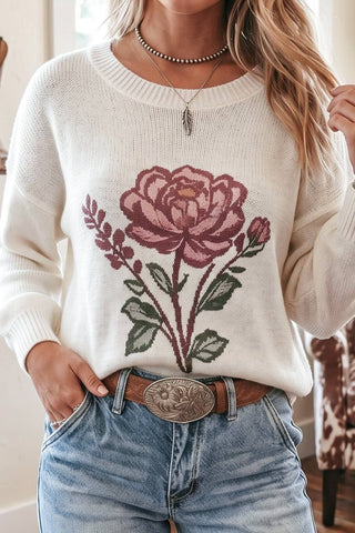 Person wearing a white sweater with a floral design and blue jeans.