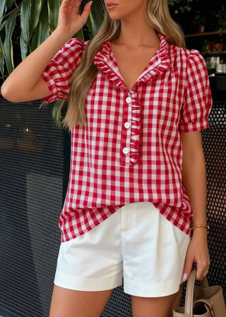 Woman wearing a red and white checkered shirt and white shorts outdoors.
