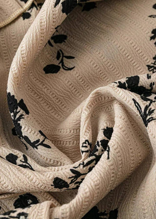 A close-up of a draped beige fabric with a textured waffle knit pattern and a black floral print.