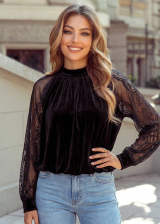 A woman wearing a black velvet mock neck top with sheer lace long sleeves, paired with light blue jeans, standing outdoors.