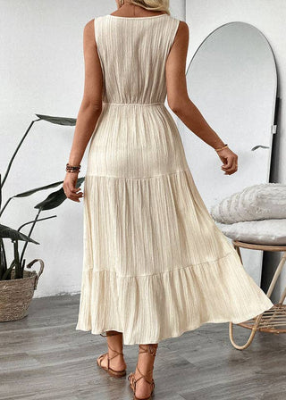 Woman wearing a beige pleated dress in a room with a plant and folded blankets.