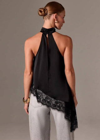Woman wearing a black halter top with lace trim and light gray pants against a beige background