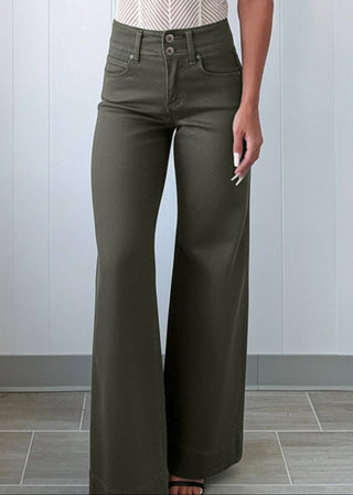 Woman wearing a white top and green high-waisted pants against a light gray wall.