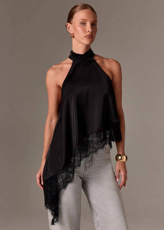 Woman wearing a black halter top with lace details and light gray pants on a plain background