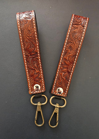 Two brown leather keychains with intricate patterns on a gray background