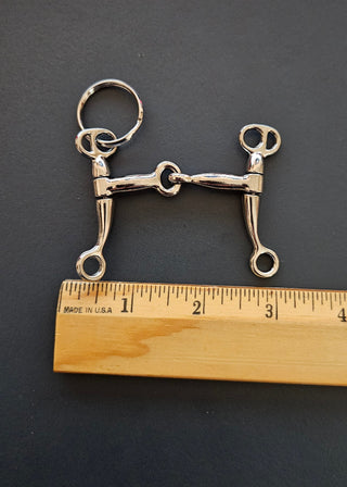 Metal horse bridle bit with a wooden ruler for scale on a dark background