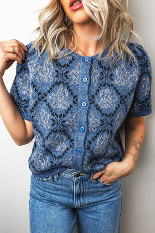 Woman wearing a blue patterned cardigan and jeans against a plain background
