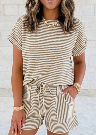 Woman wearing a striped beige and white outfit with a white brick wall background