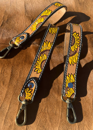 Two leather straps with sunflower patterns on a wooden surface