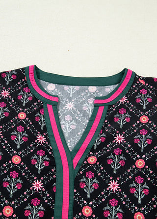 Close-up of a black embroidered tunic top featuring a vibrant pink and green border around the split neckline and a floral pattern throughout.