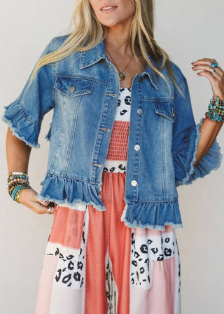 Woman wearing a denim jacket with ruffled sleeves over a colorful outfit.