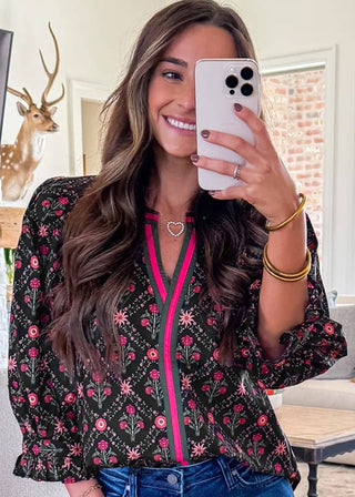 Woman taking a mirror selfie wearing a floral blouse and blue jeans in a living room.