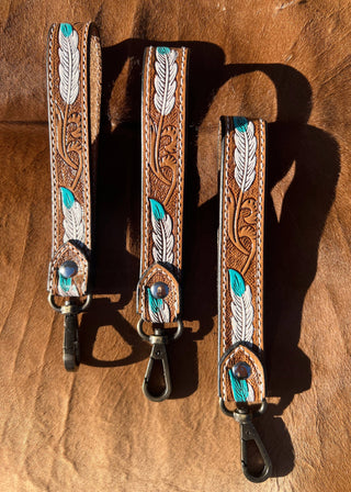 Three leather straps with feather designs on a wooden surface