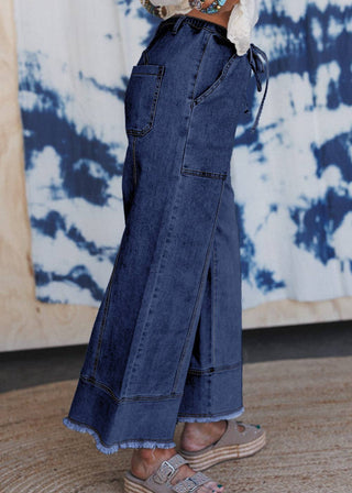 Person wearing blue denim wide-leg pants with a tie at the waist against a tie-dye background.