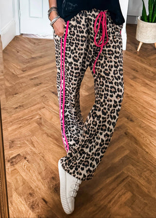 Person wearing leopard print pants with pink stripes on a wooden floor.
