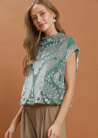 Woman wearing a green patterned top with beige pants on a brown background