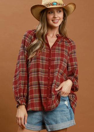 Woman wearing a red plaid shirt and denim shorts with a cowboy hat on a brown background