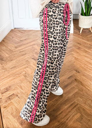 Leopard print pants with pink stripes worn by a person on a wooden floor.