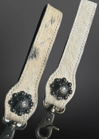 Pair of beige leather straps with metal concho embellishments on a dark background