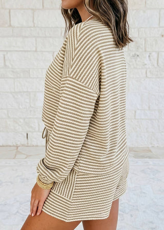 Woman wearing a beige and white striped dress against a light stone wall.