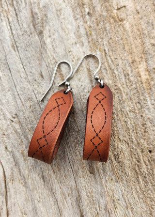 Pair of brown leather earrings with silver hooks on a wooden surface