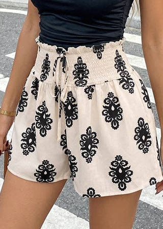 Woman wearing a black off-shoulder top and patterned shorts on a city street.