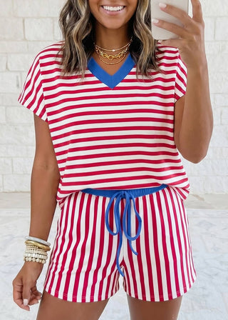 Woman wearing a red and white striped outfit with blue accents against a white brick wall.