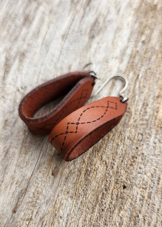 Brown leather earrings with stitching on a wooden surface
