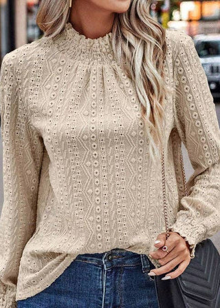 Woman wearing a beige lace blouse and blue jeans, holding a coffee cup on a city street.