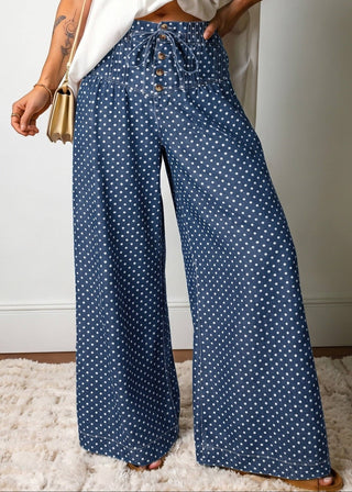 Person wearing blue polka dot pants with a white top and beige bag on a light background