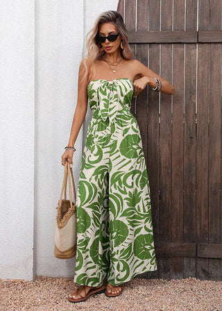 Woman wearing a strapless green leaf-patterned jumpsuit standing against a wooden door.
