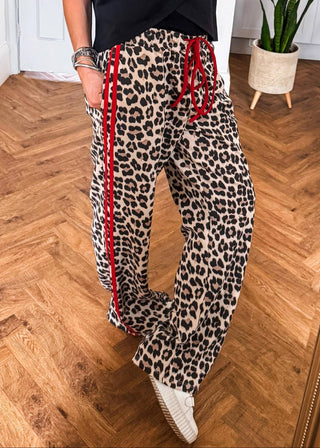 Person wearing leopard print pants with red drawstrings on a wooden floor.