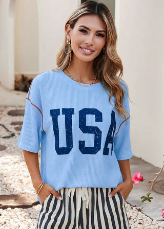 Woman wearing a blue ribbed top with bold blue “USA” lettering and red stitching