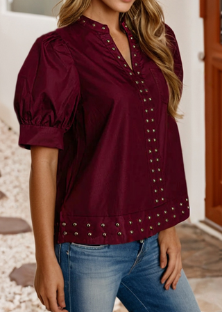 A woman wearing a burgundy short-sleeve blouse with puff sleeves and silver-tone metal studs, paired with blue jeans.