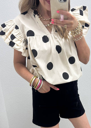 Person wearing a polka dot blouse and black shorts, taking a mirror selfie.