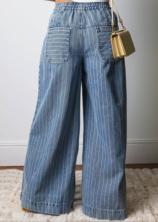 Person wearing blue pinstripe jeans holding a gold handbag against a neutral background
