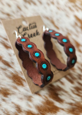 Brown hoop earrings with turquoise stones on a 'Cactus Creek' branded card, placed on a fur surface.