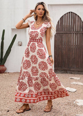 Woman wearing a red and white patterned dress standing outdoors with cacti and a wooden door in the background.