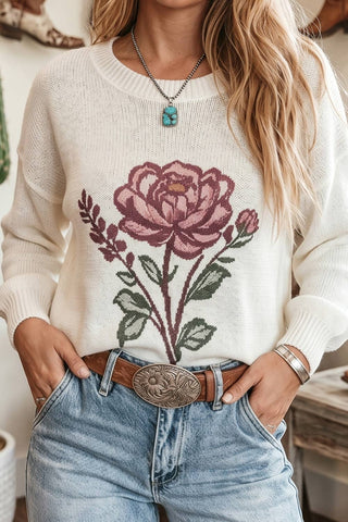 Person wearing a white sweater with a floral design and blue jeans.