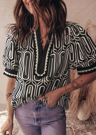 Person wearing a black and white patterned blouse with denim shorts indoors.