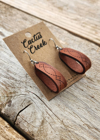 Brown leather earrings on a 'Cactus Creek' branded card, displayed on a wooden surface.