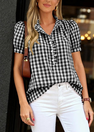 Woman wearing a black and white checkered blouse with white pants, standing against a blurred background.