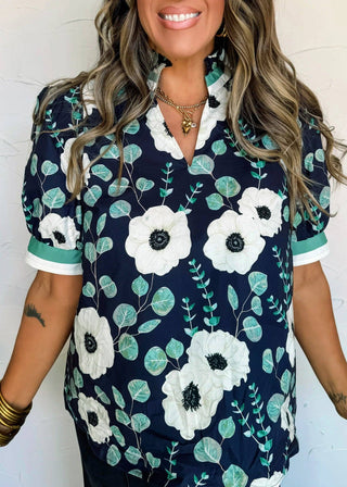 Woman wearing a navy blue floral blouse with white flowers and green leaves against a white background