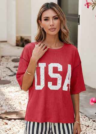 Woman wearing a red ribbed top with bold white “USA” lettering and red stitching